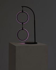 an illuminated sculpture on top of a white pedestal in front of a gray wall and floor