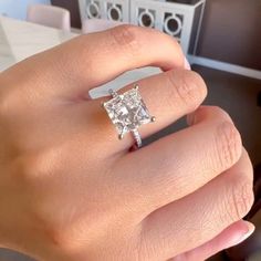 a woman's hand with a diamond ring on top of her finger, in front of a table