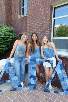 three girls standing next to each other in front of a building with letters made out of paper