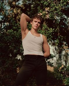 a young man posing for a photo in front of some trees with his hands behind his head