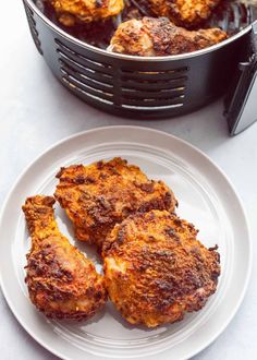 three pieces of fried chicken on a white plate next to an air frying pan