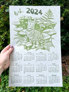 a person holding up a calendar with an owl on it in front of some bushes