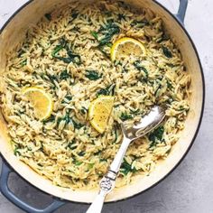 a skillet filled with pasta and spinach, topped with lemons on the side