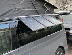 a gray van parked in front of a building with a solar panel on the roof