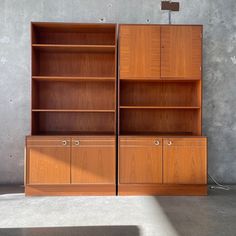 two wooden bookshelves sitting next to each other in front of a concrete wall