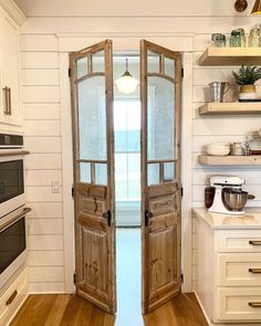 an open door leading into a kitchen with wooden floors and white walls, in front of a window