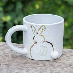 a white coffee cup with an image of a rabbit painted on the outside of it