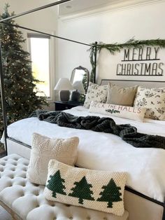 a white bed topped with pillows and blankets next to a christmas tree in a bedroom