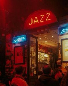 people sitting at tables in front of a restaurant with neon signs on the doors and windows