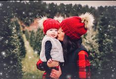 a woman holding a baby wearing a red hat while standing in front of a christmas tree