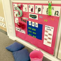 a pink bulletin board with words and pictures on it next to two blue pillows that are sitting on the floor