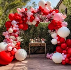 an arch made out of balloons and streamers is decorated with flowers, candles and cake