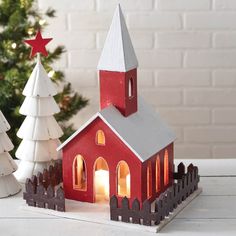 a small red church with a lit candle in front of it next to a christmas tree