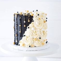 a black and white cake with gold decorations on it's sides is sitting on a pedestal