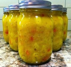 four jars filled with pickles sitting on top of a counter next to a tiled wall