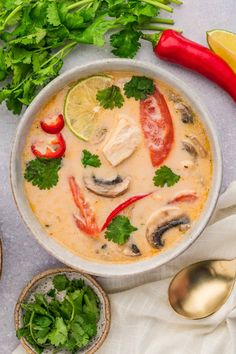 a white bowl filled with soup and garnished with cilantro, red peppers, lemon wedges and parsley