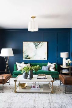 a living room with blue walls and green couches in the corner, two lamps on either side of the coffee table