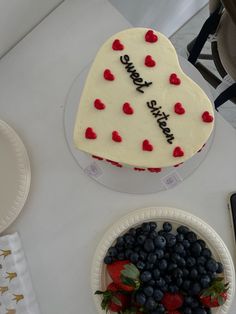 a cake with hearts and berries on it next to a bowl of strawberries