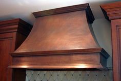 a large copper range hood mounted on the side of a wooden cabinet in a kitchen