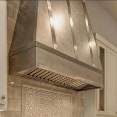 a stainless steel range hood in a kitchen with white cupboards and drawers on either side