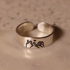 Looking for the perfect promise ring for your best friend or partner? This design features a pinky swear with two human hands, and a tiny heart above, representing the promise the ring creates. Product Details: Materials: Sterling Silver, Fine Silver, or Gold Filled Color: Silver or Gold Size: 6mm You will receive one hand-stamped ring filled with a black enamel finish. Personalized Sterling Silver Rings For Friendship, Personalized Silver Friendship Rings, Adjustable Personalized Rings For Friendship, Personalized Adjustable Rings For Friendship, Adjustable Heart Ring For Promise And Mother's Day, Adjustable Heart Ring For Promise On Mother's Day, Adjustable Minimalist Heart Ring For Promise, Adjustable Heart Toe Ring For Promise, Trendy Adjustable Heart Ring For Anniversary