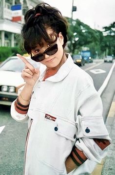 a woman standing on the side of a road holding a cell phone up to her ear