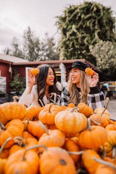 two women standing in front of a pile of pumpkins and pointing to the camera