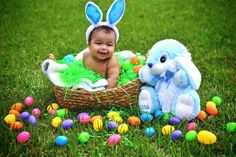 a baby sitting in a basket with an easter bunny next to it on the grass