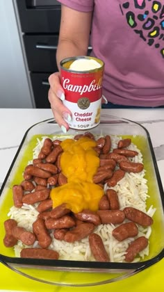 a woman holding a can of campbell's cheddar cheese sauce over rice and beans