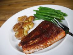 a white plate topped with meat and green beans next to potato wedges on top of a wooden table