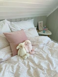 two stuffed animals sitting on top of a bed with white sheets and pink pillow cases