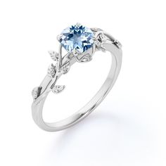 a white gold ring with an oval blue topazte and leaves on the side