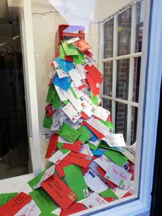 a very tall christmas tree made out of many different pieces of paper on the window sill