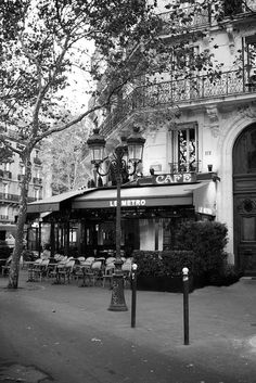 a black and white photo of the outside of a building with tables and chairs in front of it