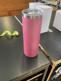 a pink tumbler cup sitting on top of a table next to a measuring tape