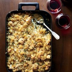 a casserole dish with meat and vegetables in it next to two glasses of wine