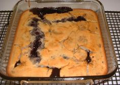 a baked dessert in a baking pan on a cooling rack with chocolate sauce drizzled over the top