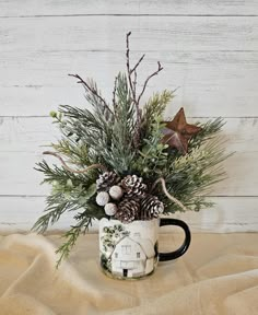 a coffee mug filled with pine cones and greenery on top of a tablecloth