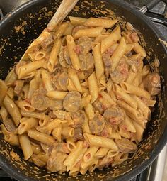 a skillet filled with pasta and meat on top of a stove next to a wooden spoon