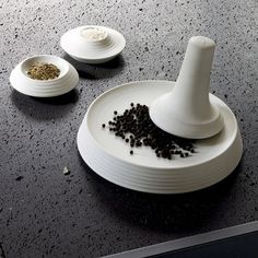 two white bowls with black seeds on them and one is filled with seasoning next to a salt shaker