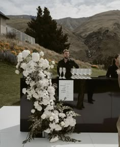 a man standing behind a black counter with white flowers on it next to a woman