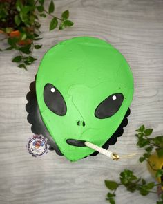 a green alien mask sitting on top of a table next to a plant and a stick