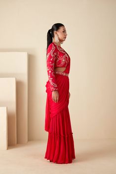 This ensemble features a pre-draped sharara saree in a vibrant red hue, adorned with exquisite craftsmanship. Paired with a beautifully handcrafted blouse, boasting a crew neckline and full sleeves, it exudes sophistication with every detail. The ensemble is accentuated with a separate belt, enhancing its elegance. Crafted from luxurious georgette crepe, both the saree and blouse are meticulously designed for comfort and style, with the blouse lined for added comfort. The back oval cutout adds a Blouse And Sharara, Red Sharara, Sharara Saree, Dhoti Saree, Western Gown, Indo Western Gown, Saree And Blouse, Full Sleeve Blouse, Pleated Drapes