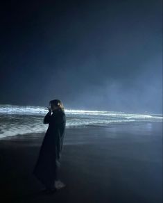 a woman standing on the beach at night talking on her cell phone while looking out to sea