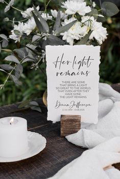 a table topped with white flowers next to a candle and a sign that says her light remains