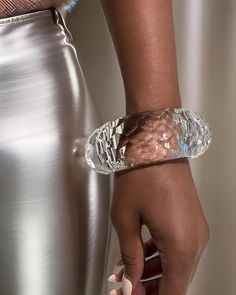 Close-up of a person’s hand wearing a large, clear, hand-sculpted Croc Lucite Cuff Bracelet by Nik Spruill, with a metallic skirt visible in the background. Round Lucite Jewelry For Parties, Luxury Cuff Bracelet For Parties, Luxury Cuff Bangle Bracelet For Party, Modern Resin Jewelry For Parties, Modern Resin Jewelry For Party, Luxury Glass Jewelry For Party, Elegant Resin Jewelry For Party, Clear Lucite Party Jewelry, Modern Clear Bracelet Jewelry