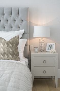 a white bed sitting next to a night stand with a lamp on top of it