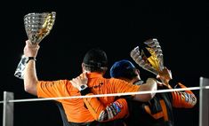 two men are hugging each other while holding trophies in their hands and wearing orange shirts