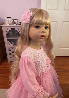 a doll with blonde hair and blue eyes wearing a pink dress in front of a white door