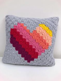 a crocheted heart pillow is shown on a white surface with a pink, yellow, red and orange pattern